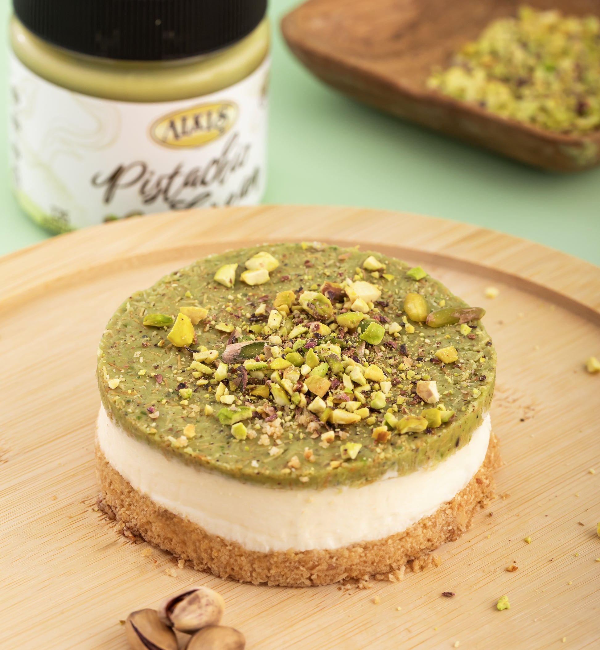 Green dessert with pistachios on a wooden board next to a jar of pistachio spread.