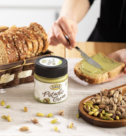 Person spreading pistachio cream on bread with a jar of Alnus Pistachio Cream in the foreground.