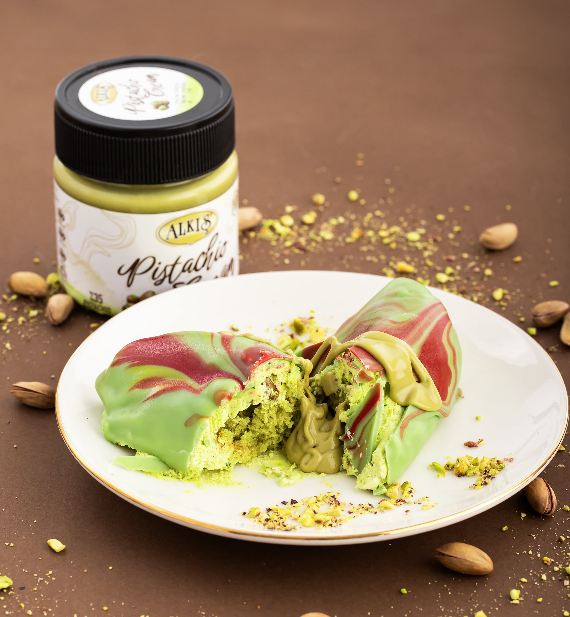 Pistachio-flavored dessert on a plate with a jar of Alki's Pistachio spread in the background.